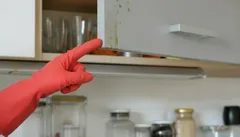 Ręka w czerwonej rękawiczce wskazuje brud na szafce kuchennej