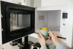 Otwarta mikrofalówka, osoba wkłada kubek z cytryną do środka w kuchni.