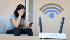 Kobieta sfrustrowana problemem z WiFi, siedzi obok routera i trzyma smartfona