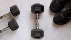 Hantle i buty sportowe na jasnej podłodze, sprzęt do ćwiczeń fitness w domu lub na siłowni.